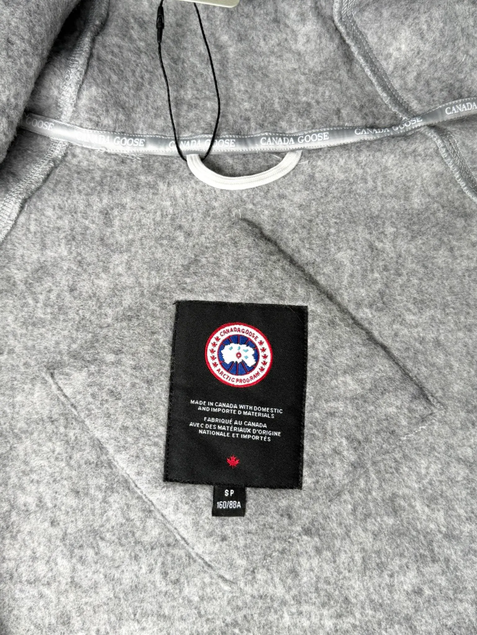 P660 Canada Goose Fleece Wool Badge Hooded Jacket Fabric selection: Wool fleece fabric blended with wool as the main body and a very small amount of spandex and polyester fiber. Wool is a core natural ingredient that provides unparalleled temperature regulation, antibacterial and anti-odor properties and a skin-friendly feel. The feeding of a small amount of spandex gives the fabric a certain degree of four-way elasticity, making it non-restrictive during daily activities. As the basis of fleece's structure, polyester fiber enhances the fabric's durability, wrinkle resistance and quick-drying properties. It contributes to the loft of the fleece and provides functions such as trapping air.  Detail 1: The sleeves and hem are closed with 2×2 ribbing. Its strong elasticity can closely fit wrists and waists of different thicknesses, forming an effective 'seal' to prevent cold wind from blowing back. It can still maintain its original shape after repeated stretching and use, and is not easy to loose and deform. And the ribbed cuffs can convey a sense of design and enhance the visual beauty.  Detail 2: The combination of hood design and elastic buckle improves warmth and windproof performance when wearing. Accessories: Customized elastic drawstring, elastic buckle, custom zipper pendant, custom armband Size: S M L Color: black gray coffee rice pink